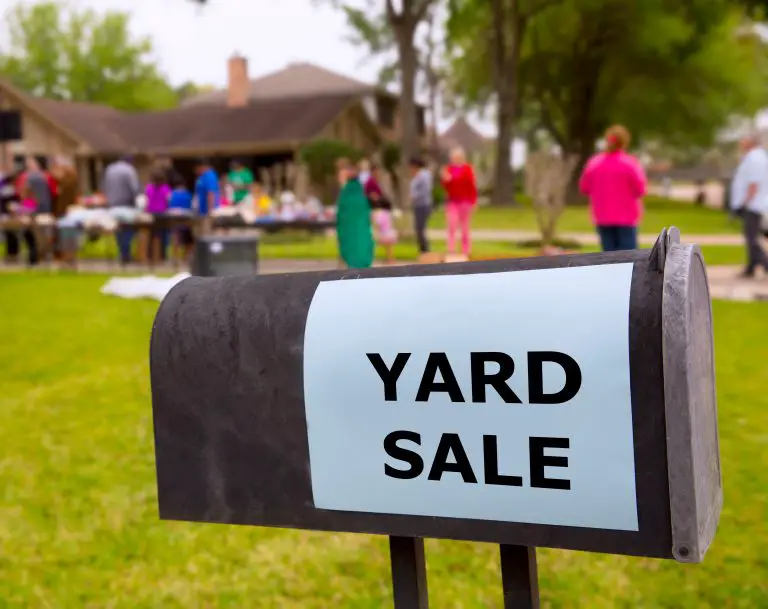 yard sale sign on a mailbox with people browsing in the background